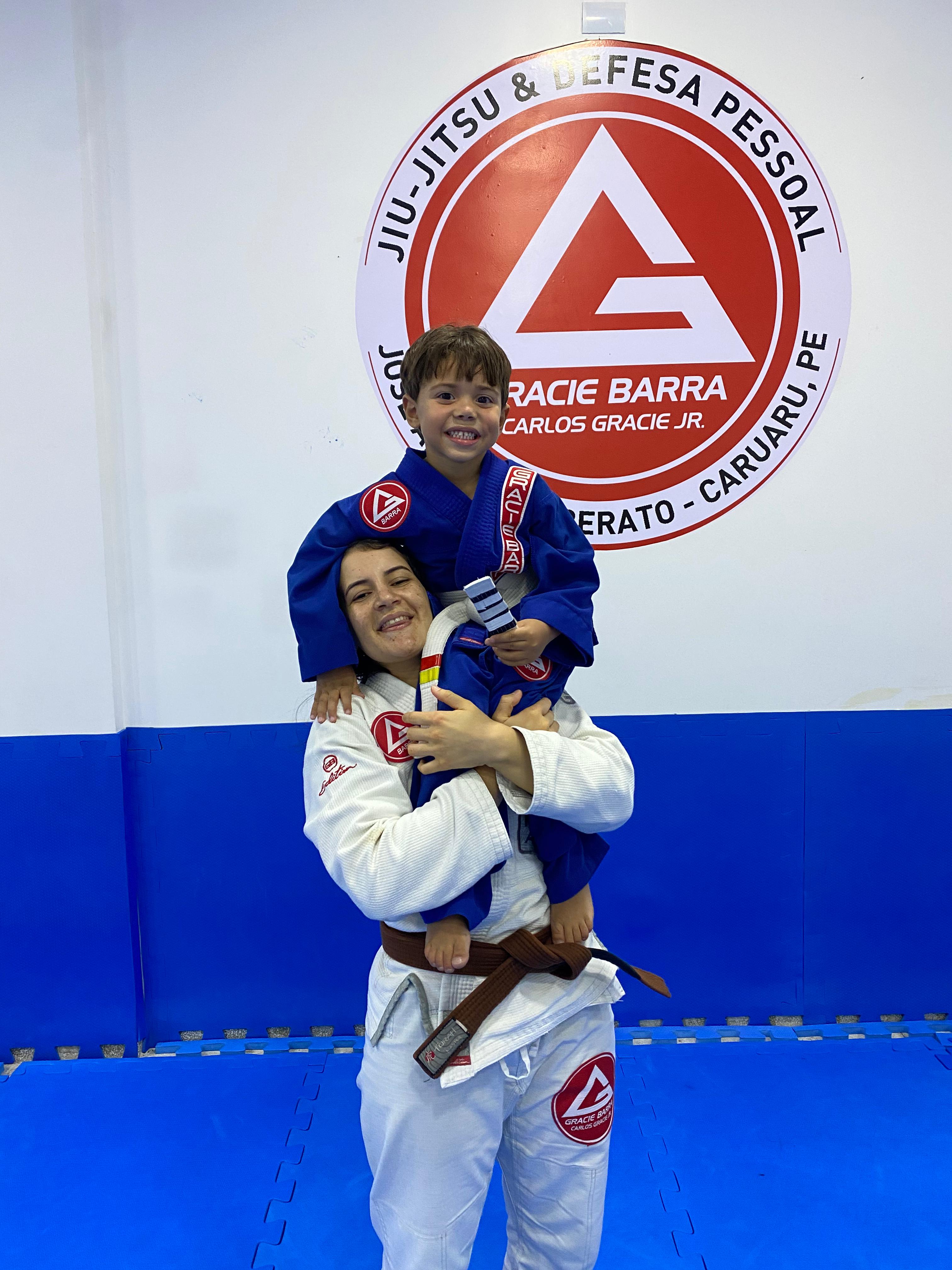 Karyne carregando criança no colo em frente ao logo Gracie Barra Caruaru