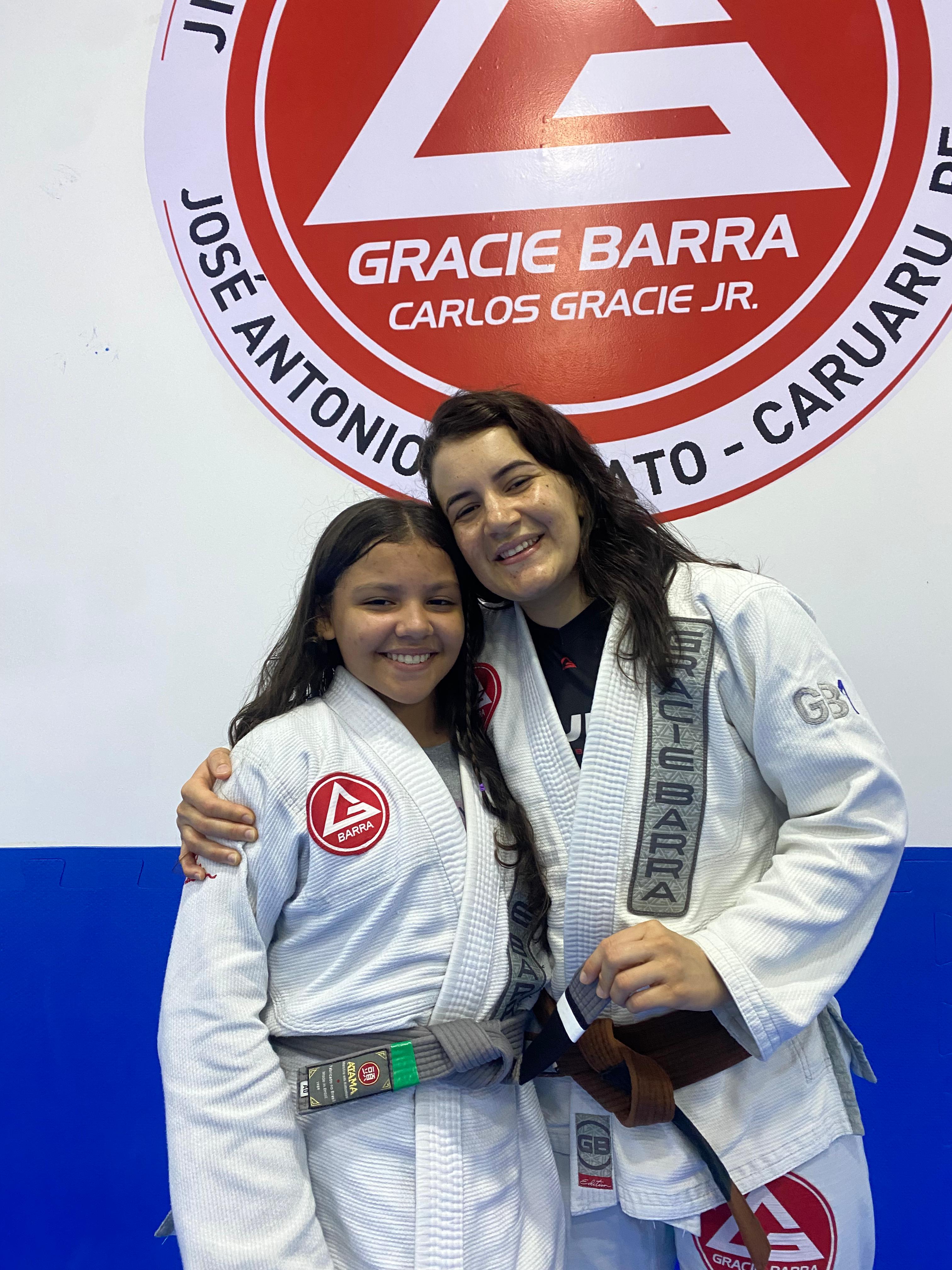 Karyne com aluna infantil em frente ao logo Gracie Barra Caruaru
