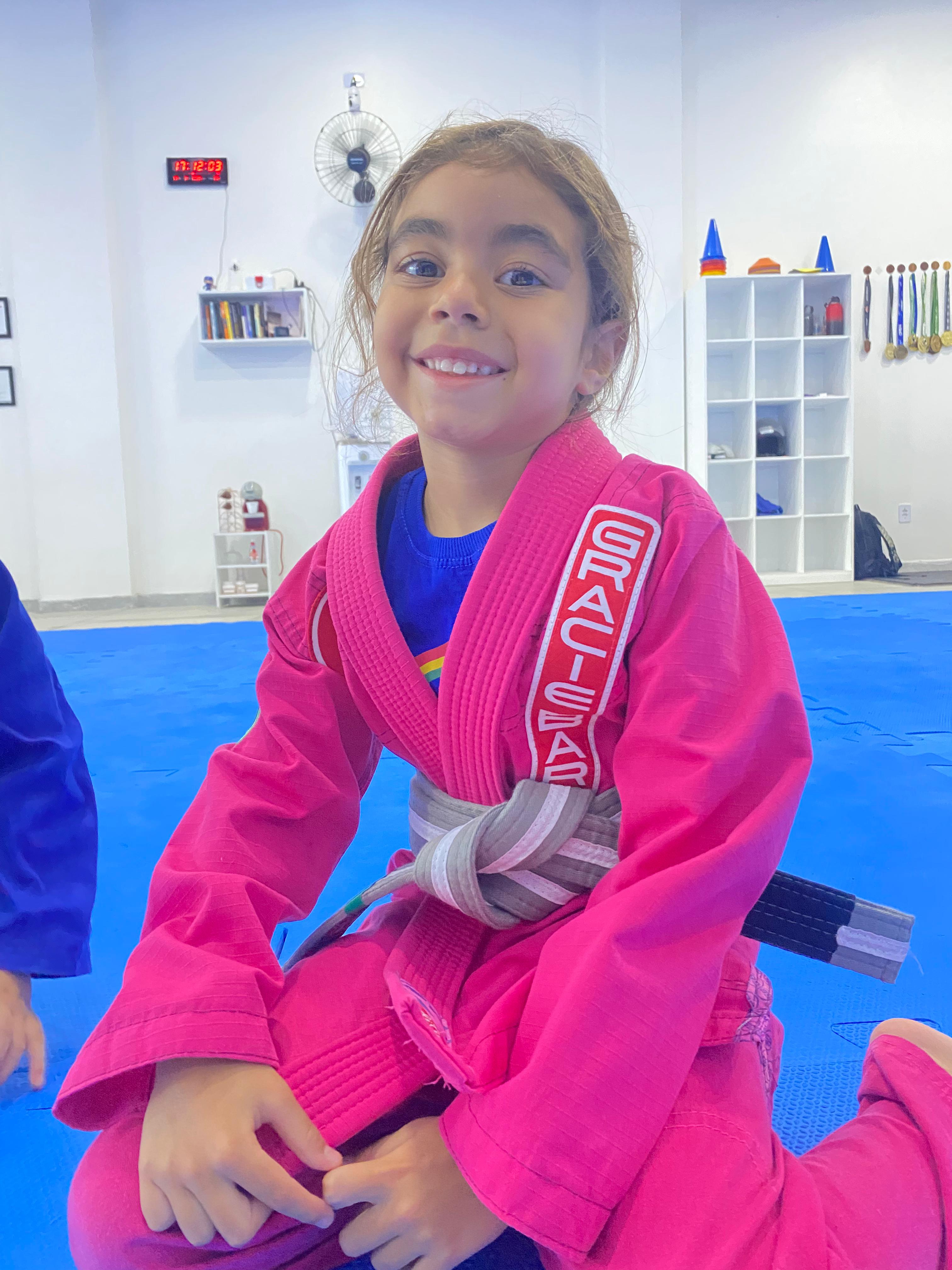 Aluna do programa infantil sorrindo em kimono rosa Gracie Barra