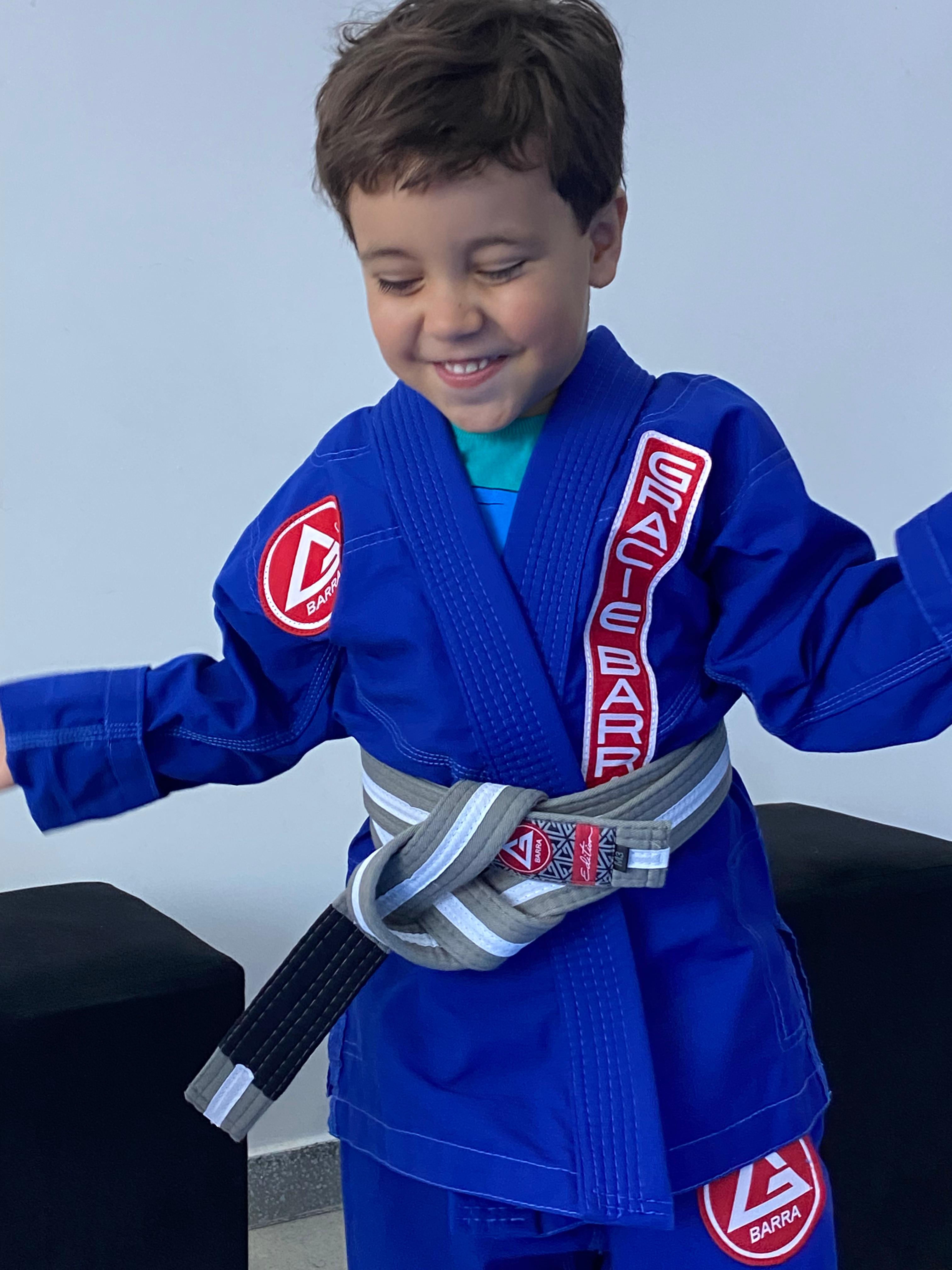Aluno do programa infantil sorrindo em kimono azul Gracie Barra