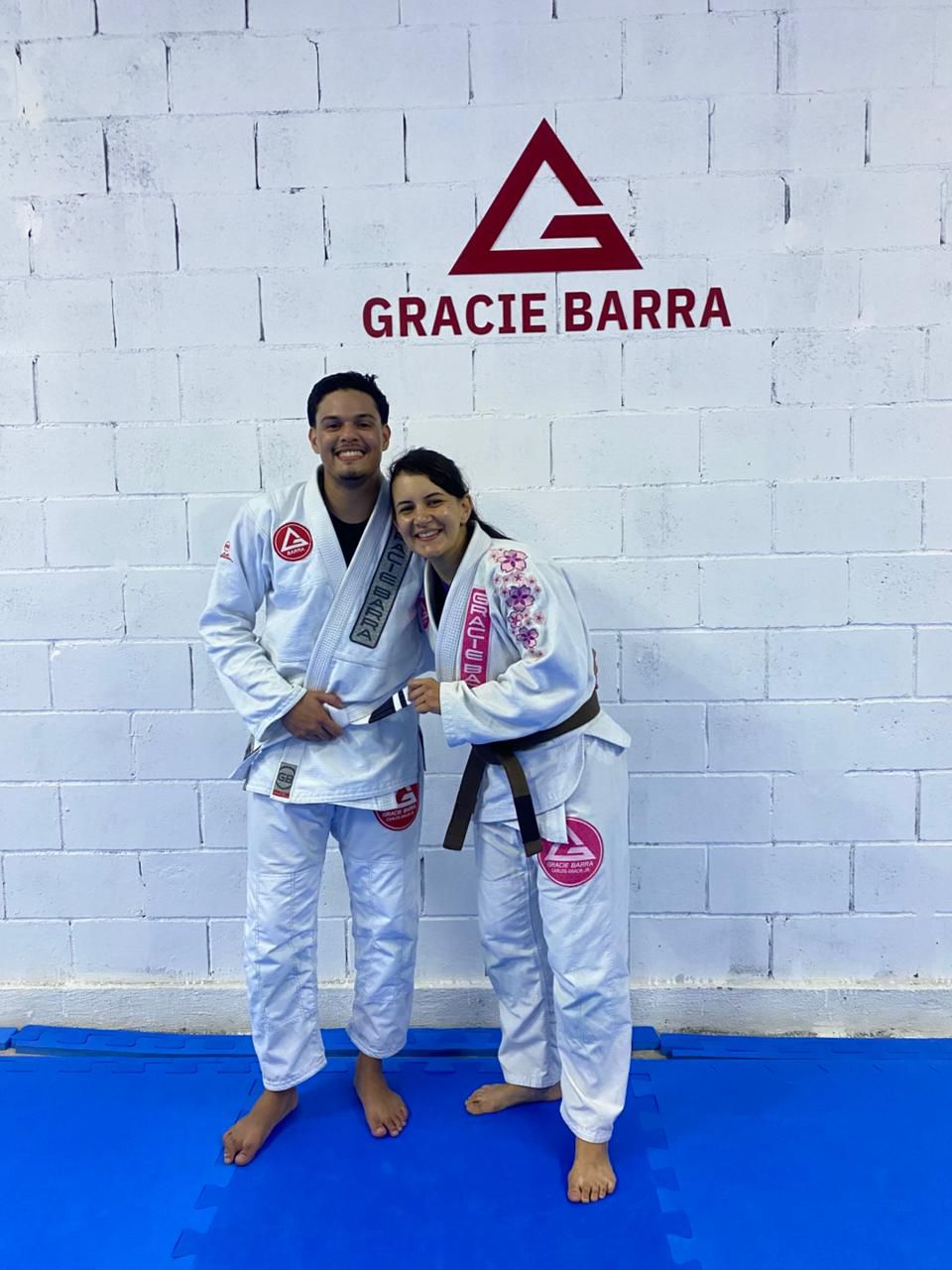 Professor e aluna posando em frente ao logo da Gracie Barra Caruaru